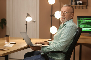 mature programmer working with laptop at office in evening