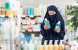 © JackF - Female shopper dressed in traditional Islamic clothing comparing two mouthwash products while standing in personal care section of drugstore....
