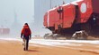 © NArts - A solitary figure walks a snowy, desert path, towards large, red vehicles.
