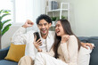 © Pormezz - Relax and happiness lifestyle at home concept. Young couple sitting on sofa in living room looking at smartphone smile on face in cozy atmosphere.
