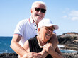 © luciano - Joyful senior couple enjoys a beautiful day by the ocean, hugging each other with smiles. Background of rocky coastal landscape, a perfect scene of love, companionship and happiness in retirement