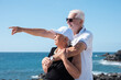 © luciano - Carefree senior couple enjoys a beautiful day by the ocean, hugging each other with smiles. Background of rocky coastal landscape, a perfect scene of love, companionship and happiness in retirement