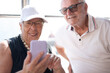 © luciano - Elderly pensioner couple joyfully sharing a digital moment looking at smartphone together. Modernity, friendship, positivity and companionship concept, staying connected in the digital age