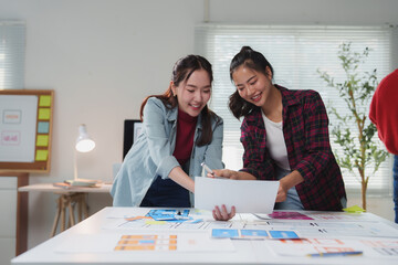 Wall Mural - two young female web designers are smiling while working together on a new project, analyzing and di