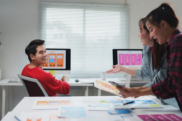 Wall Mural - asian uiux designers collaborating and discussing mobile app interface wireframe designs in a modern