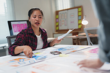Wall Mural - asian female web designer collaborating with a colleague in a modern office, discussing mobile app u