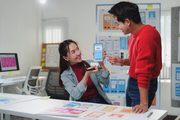 Wall Mural - two young asian user experience designers are collaborating on a mobile app interface, holding a sma