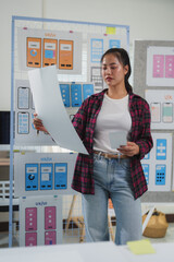 Wall Mural - female ux ui designer comparing mobile application wireframe sketches and layouts, working on user i