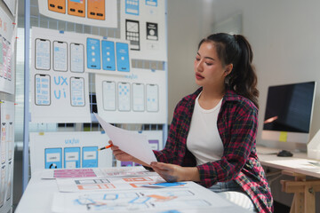 Wall Mural - asian female web designer working on user interface and user experience design of a mobile app and w