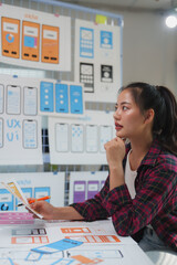 Wall Mural - female web designer analyzing mobile application interface wireframes, holding a pen and thinking ab