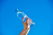 © licvin - A girl holds a bottle of drinking water in her hand against a blue sky background