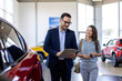 © Graphicroyalty - Super sales team, man and woman, in dealership, two consultants or managers in elegant suits with laptop and tablet in arms in car dealership