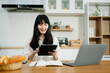© Nuttapong punna - Woman using laptop while sitting at home. Young woman sitting in kitchen