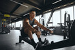 © Davidovici - Determined attractive male using rowing machine in contemporary gym. Fit young man working out on rowing equipment at fitness center. Weight loss and cardio exercise concept
