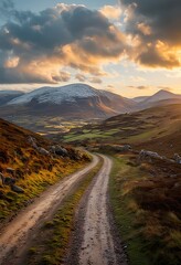 Wall Mural - a winding dirt road leads towards snow-capped mountains under a dramatic and golden sunset sky in the irish countryside.