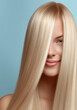 © southwind - Beautiful blonde woman showing long straight healthy hair on blue background