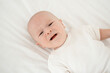 © Any Grant - a crying baby in a white bodysuit on the bed at home, a close-up portrait of a crying baby, a small child calling his mother, a place for text