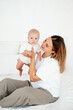 © Any Grant - a young beautiful mother with a baby boy hugging on the bed at home in the bedroom, mother's care and love, portrait of a happy mother with a child, healthy motherhood