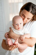 © Any Grant - mom and baby, mom holds the baby's legs in her tender hands, mother hugs and kisses at home in the child's bedroom, maternal care and love, portrait of a happy mother with a child, legs in focus