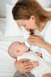 © Any Grant - mom feeds the baby with a bottle of milk or formula, feeding the baby in her arms, a young mother feeds the newborn baby at home on the bed
