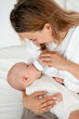 © Any Grant - mom feeds the baby with a bottle of milk or formula, feeding the baby in her arms, a young mother feeds the newborn baby at home on the bed