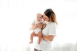 © Any Grant - happy mom with a newborn baby on a white isolated background, space for text, mom hugs and kisses her baby while holding him in her arms, happy motherhood
