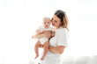 © Any Grant - happy mom with a newborn baby on a white isolated background, space for text, mom hugs and kisses her baby while holding him in her arms, happy motherhood