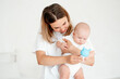 © Any Grant - mom and baby, mother hold a newborn baby in her arms at home in the bedroom, hugging him, playing with him with a rattle, maternal care and love, portrait of a happy mother with a child.