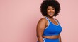 © Cintia - Smiling woman in blue athletic wear poses against pink backdrop with curly hair.