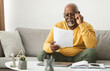 © Prostock-studio - Senior African American Male Working With Papers Wearing Eyeglasses Sitting On Couch At Home. Professional Freelancer Doing Paperwork. Freelance Career Concept. Selective Focus
