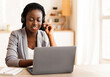 © Prostock-studio - Call center operator at work. Beautiful afro female manager wearing headset and typing at laptop, consulting clients, working in modern office.