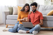 © Prostock-studio - Smiling Indian Couple With Laptop And Coffee Relaxing In Living Room At Home, Happy Young Eastern Spouses Resting On Floor And Using Computer Together, Shopping Online Or Browsing Internet