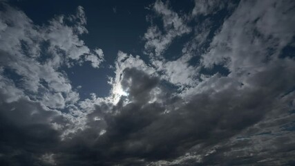 Wall Mural - Time lapse looking towards the sun of dramatic gray clouds moving through a dark blue summer sky. Isolated to sky only.
