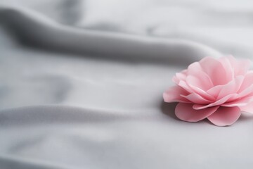 Poster - Delicate pink camellia with glistening dewdrops on its petals rests on soft gray fabric, offering a serene and elegant floral design element with copy space