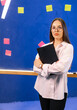© Vadim - Confident young pro with notebook. A focused young woman dressed in a light shirt looks towards the camera, holding a notebook in front of a colorful wall.