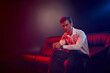 © LIGHTFIELD STUDIOS - Handsome young man in stylish attire poses confidently on modern couch in dramatic lighting