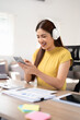 © Fahng - Business woman with laptop using mobile phone and listening music through headphones at home office.