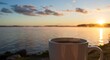 © Yshfrn - A white cup of coffee steams gently at sunrise, overlooking calm water reflecting light.