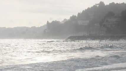 Wall Mural - foaming white waves breaking against rocky coastline of estoril, portugal, with coastal buildings an