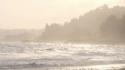Wall Mural - golden sunlight bathing rocky shoreline, illuminating breaking waves crashing against sandy coast du