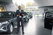 © Oleksii Syrotkin/Stocksy - Cheerful sales agent posing among brand-new vehicles in showroom