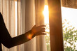 © Photo Sesaon - woman's hand She opened the curtains on the window. There was morning light through the window in her room, looking at the view of the mountains and trees as the sun rose