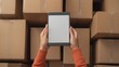 © PStyle - A person holds a tablet with a blank screen in front of stacked cardboard boxes, suggesting inventory or shipping management.