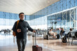 © Hernandez & Sorokina/Stocksy - Man walking in airport holding phone and suitcase
