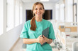 © Santi Nuñez/Stocksy - Smiling doctor wearing green scrubs holding tablet in hospital