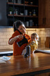 © Jovo Jovanovic/Stocksy - Mother is using phone and pouring coffee while carrying daughter