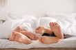 © Pixel-Shot - Feet of young man with two women lying under blanket in bedroom, closeup. Polyamory concept