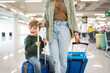 © Santi Nuñez/Stocksy - Happy child sitting on suitcase at airport with mother