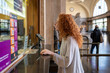 © Miquel - Young woman buying train ticket at ticket office window in train station