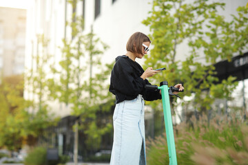 stylish young woman with smartphone scans qr code for electric scooter rental. girl using app on pho
